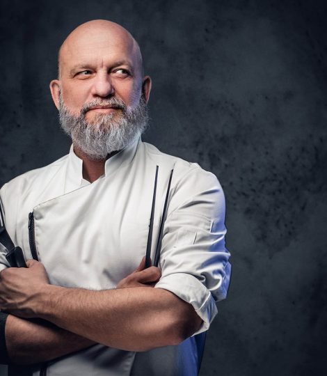 shot-of-professional-old-chef-dressed-in-uniform-holding-kitchen-spatula-and-tongs